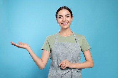 Photo of Young woman in grey apron on light blue background,