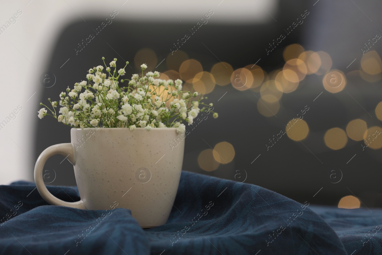 Photo of Cup with tiny flowers on soft knitted blanket against blurred lights. Space for text