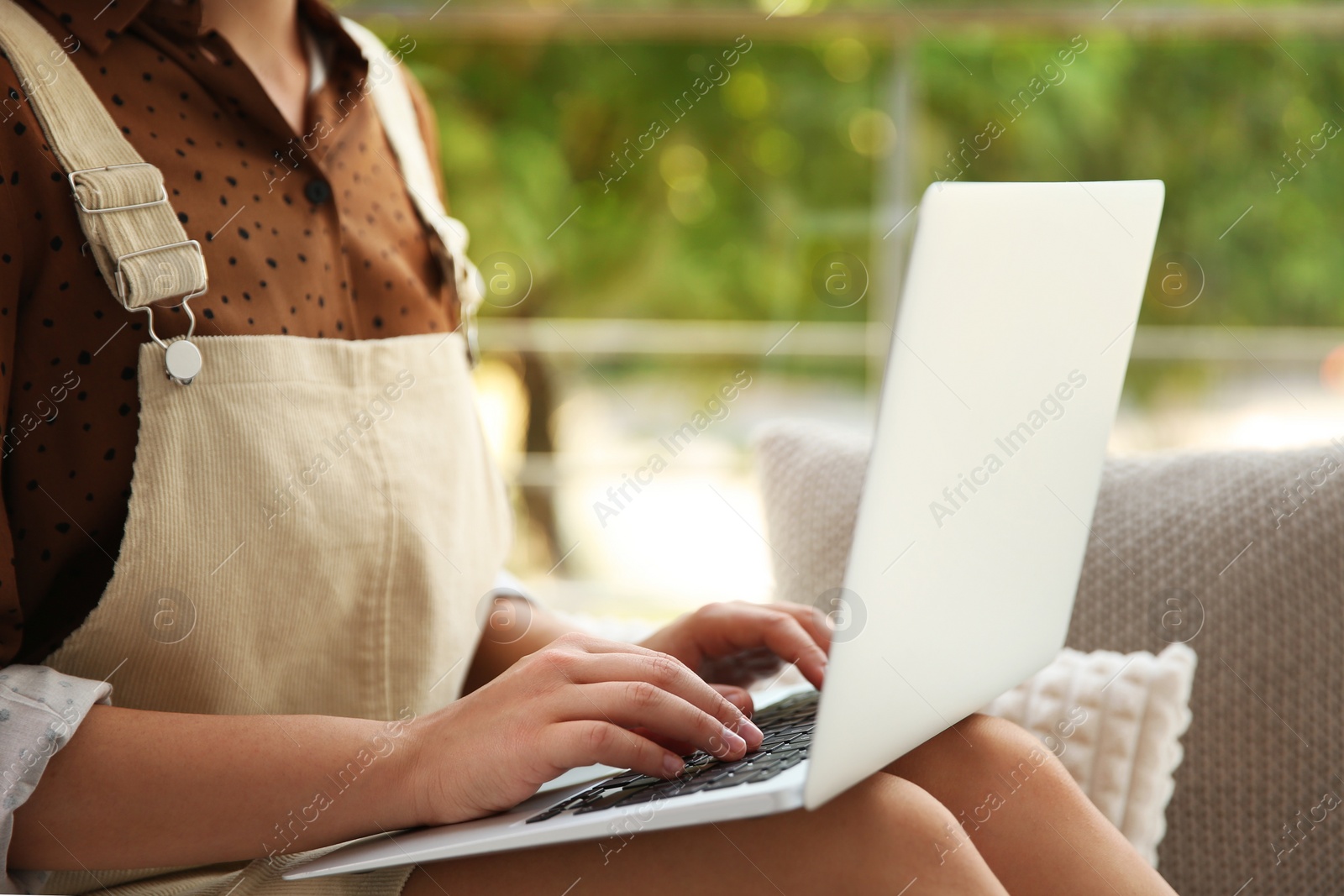 Photo of Young woman working with laptop near window at home office, closeup