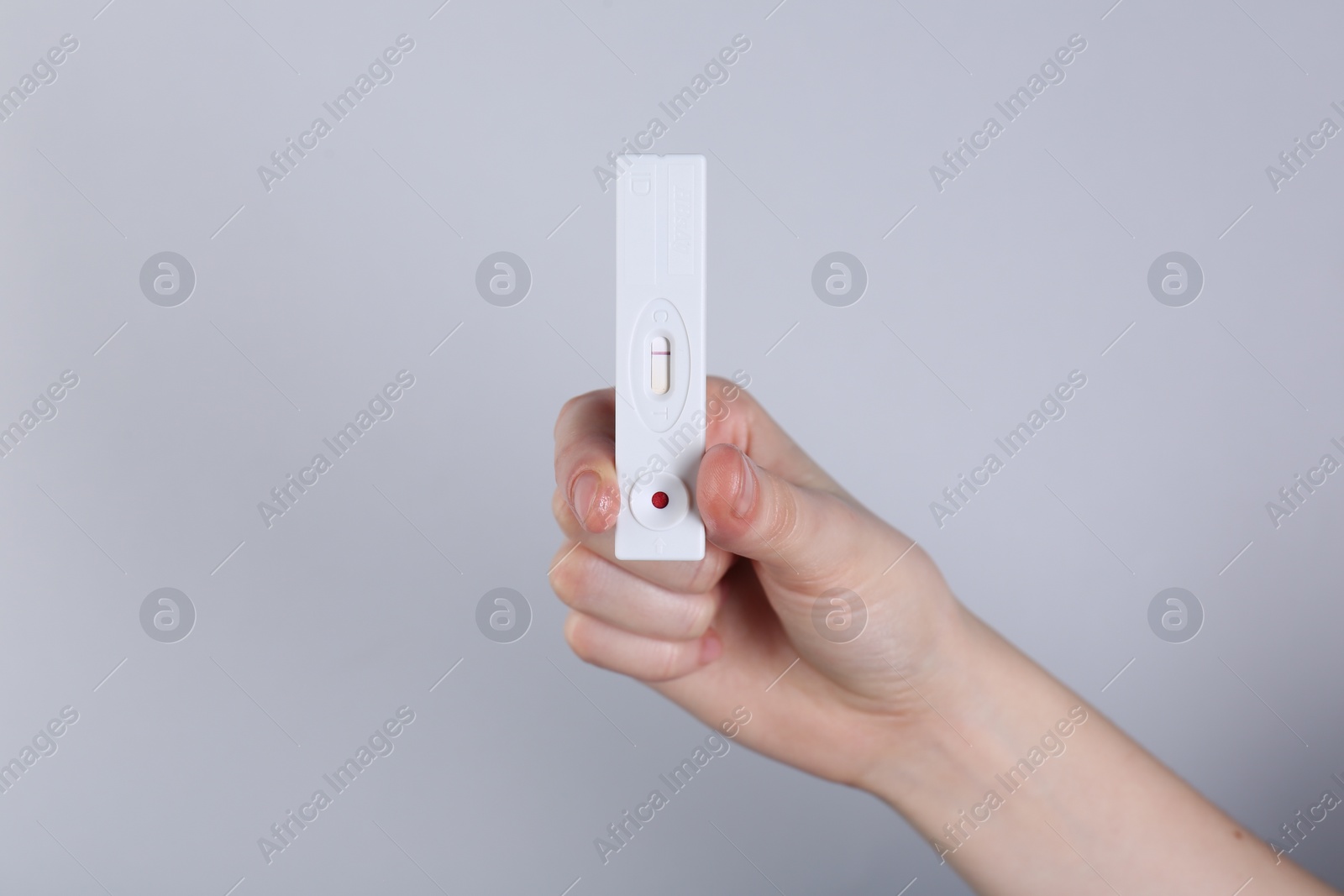 Photo of Woman holding disposable express test on light grey background, closeup