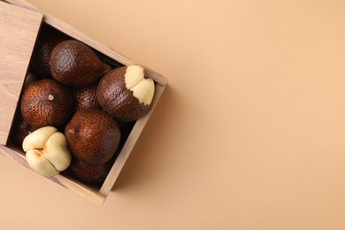 Photo of Wooden crate with fresh salak fruits on beige background, top view. Space for text