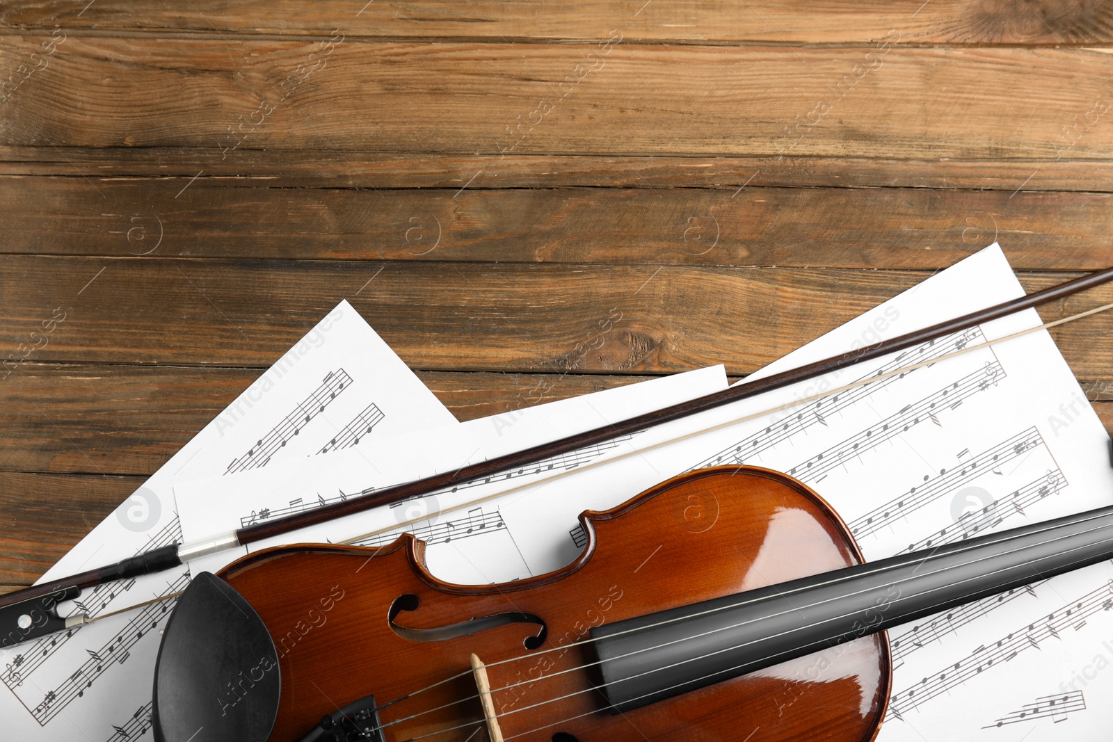 Photo of Beautiful violin, bow and note sheets on wooden table, flat lay. Space for text