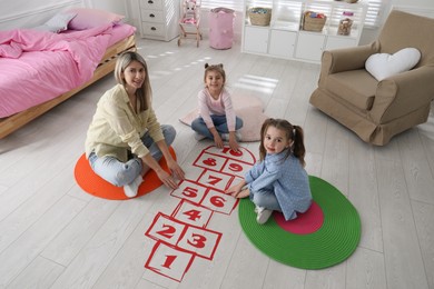 Photo of Mother and little girls taping sticker hopscotch on floor at home