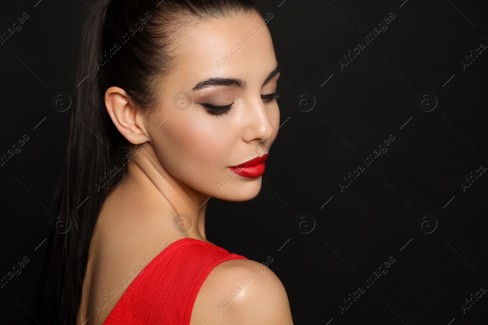 Photo of Portrait of young woman wearing beautiful red lipstick on black background, space for text