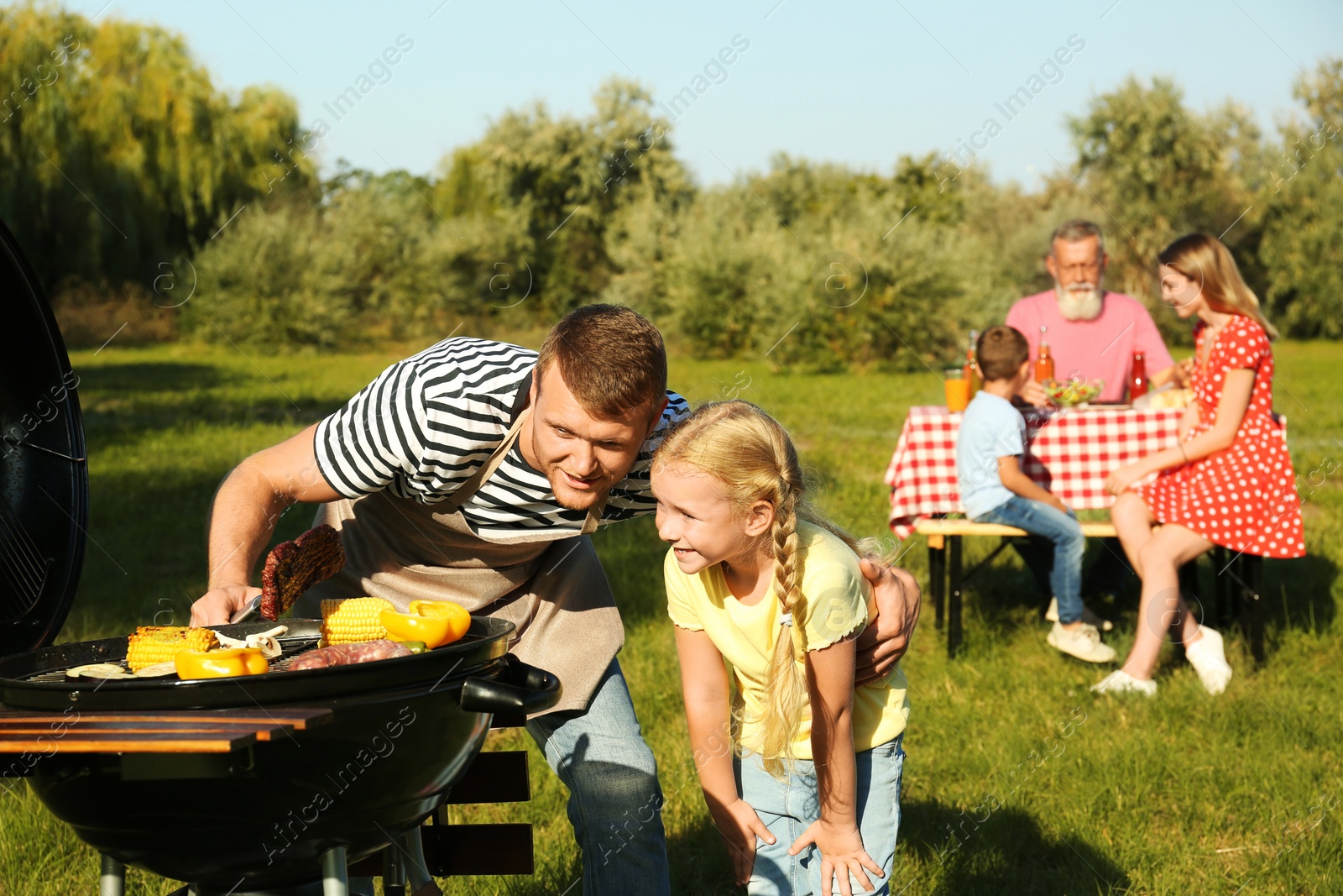 Photo of Father with little girl at barbecue grill and their family in park