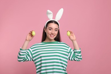 Photo of Happy woman in bunny ears headband holding painted Easter eggs on pink background