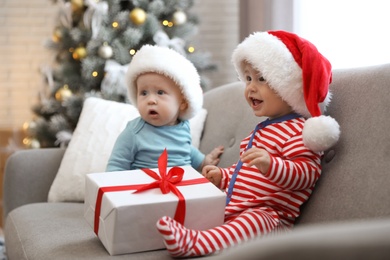 Cute children in Santa hats sitting on sofa at home. Christmas celebration