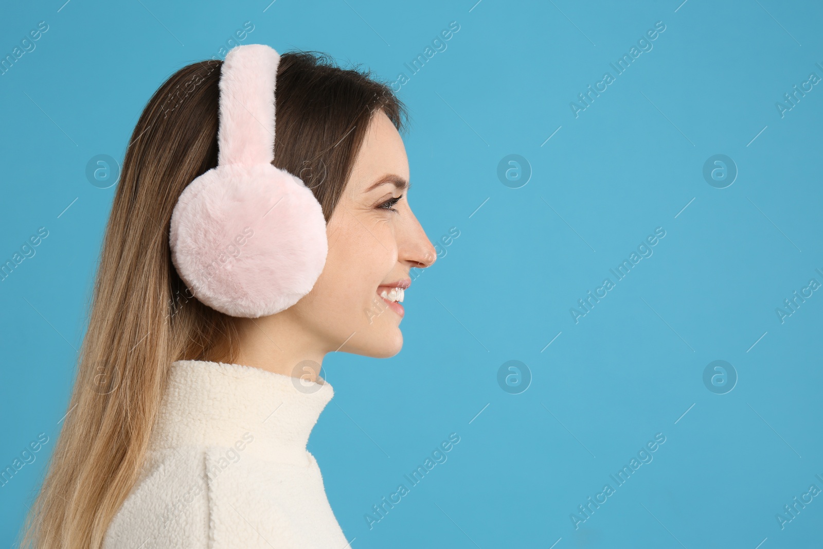 Photo of Happy woman wearing warm earmuffs on light blue background, space for text