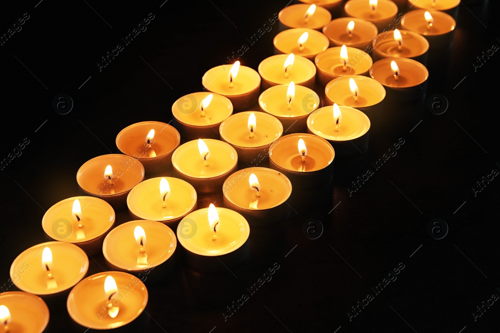 Photo of Wax candles burning on table in darkness, closeup