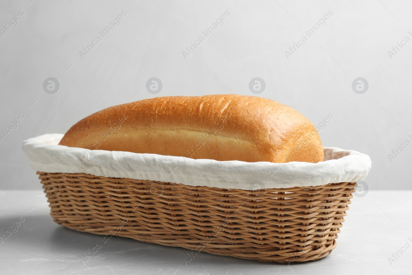 Photo of Loaf of tasty fresh bread in wicker basket on light marble table