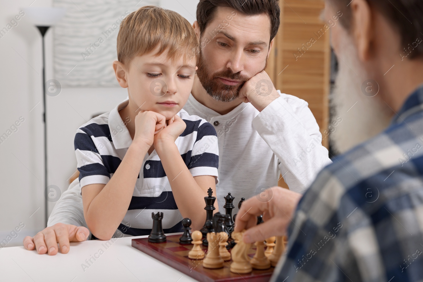 Photo of Family playing chess together at table in room