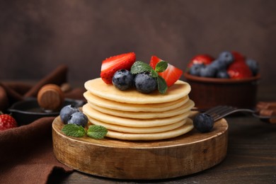 Photo of Delicious pancakes with strawberries, blueberries and mint on wooden table, closeup