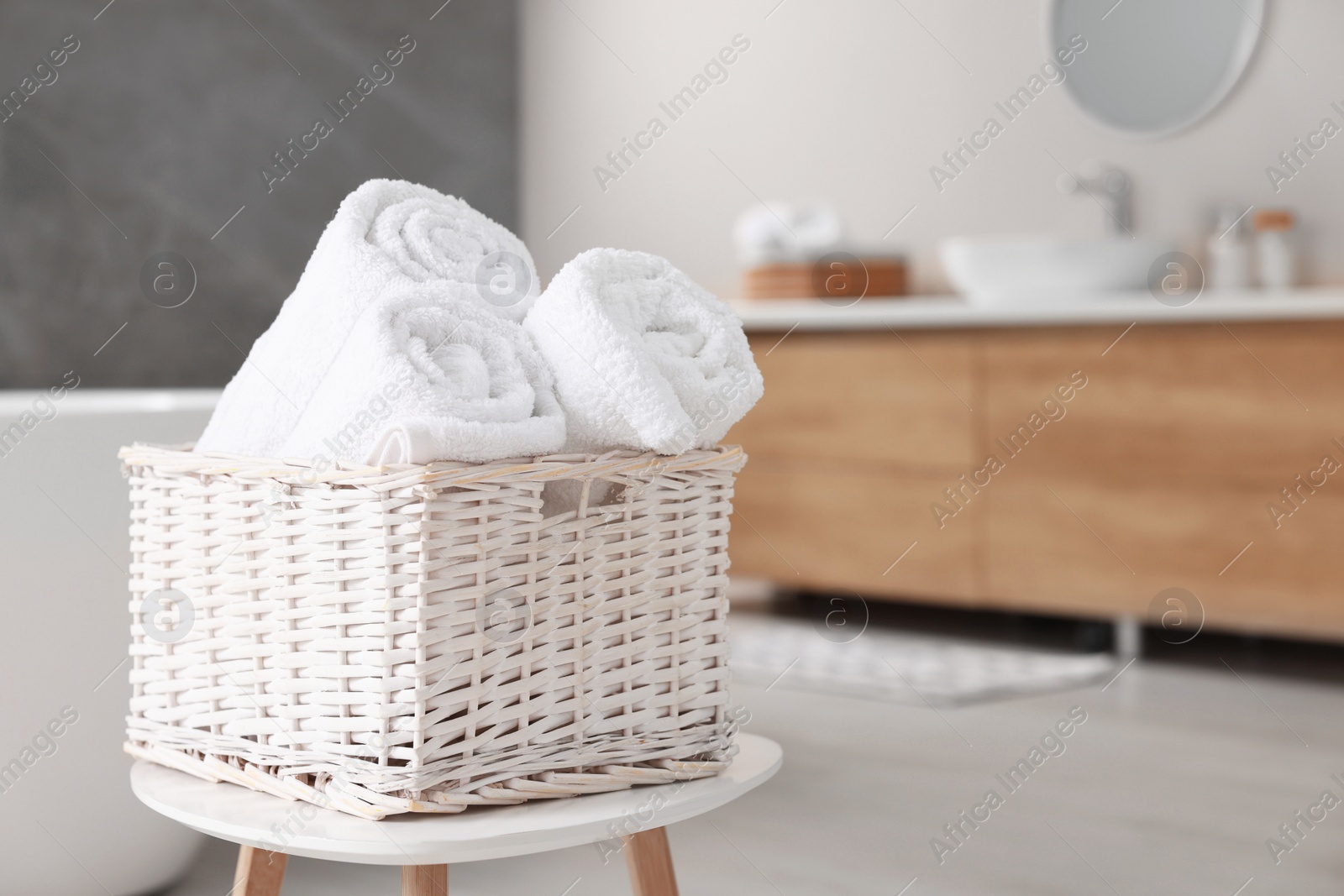 Photo of Wicker basket with fresh white towels on stool in bathroom. Space for text