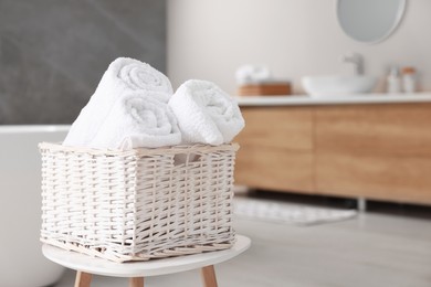 Photo of Wicker basket with fresh white towels on stool in bathroom. Space for text