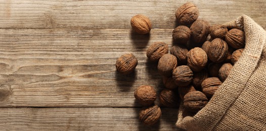 Burlap sack with walnuts on wooden table, top view. Space for text