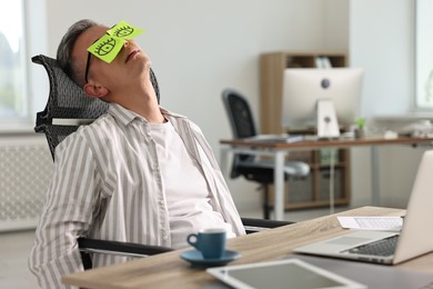 Man with fake eyes painted on sticky notes snoozing at workplace in office