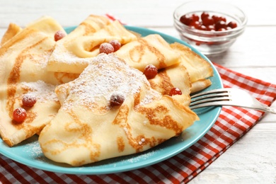 Photo of Thin pancakes served with sugar powder and berries on plate, closeup