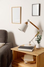 Photo of Stylish modern desk lamp, book and plant on wooden cabinet near white wall indoors