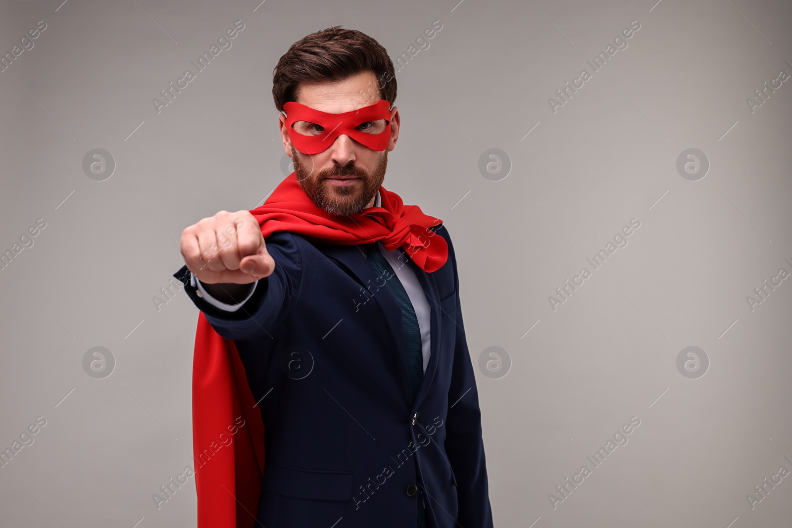 Photo of Confident businessman wearing red superhero cape and mask on beige background