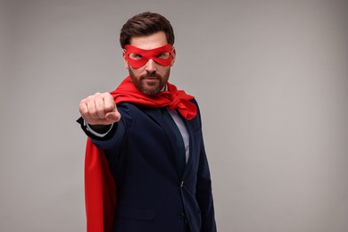 Confident businessman wearing red superhero cape and mask on beige background