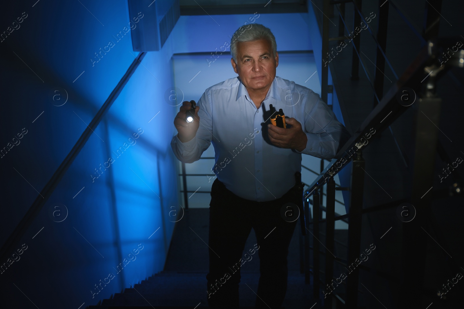 Photo of Professional security guard with flashlight on stairs in dark room