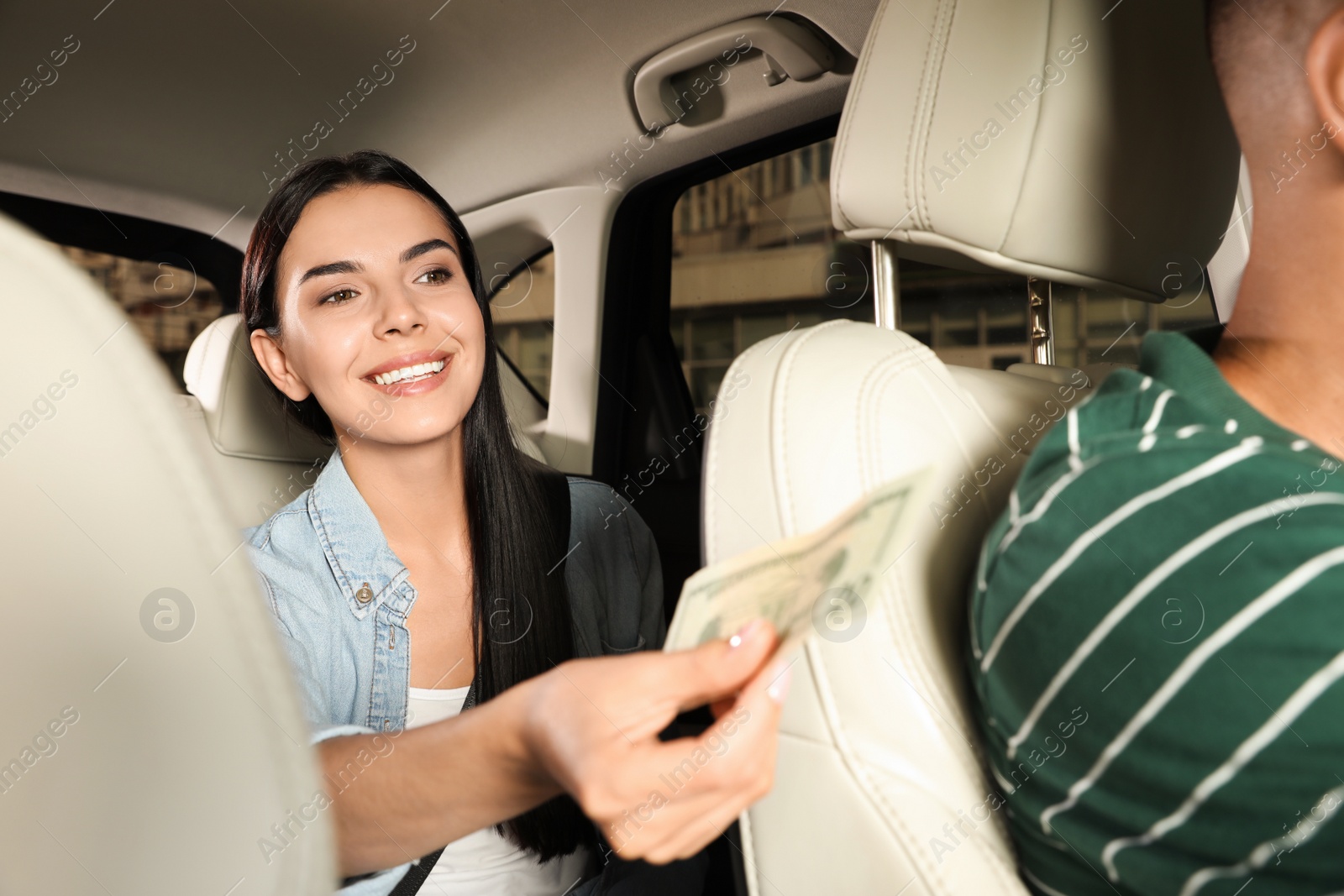 Photo of Young woman giving money to taxi driver in modern car