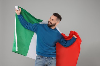 Young man holding flag of Italy on light grey background