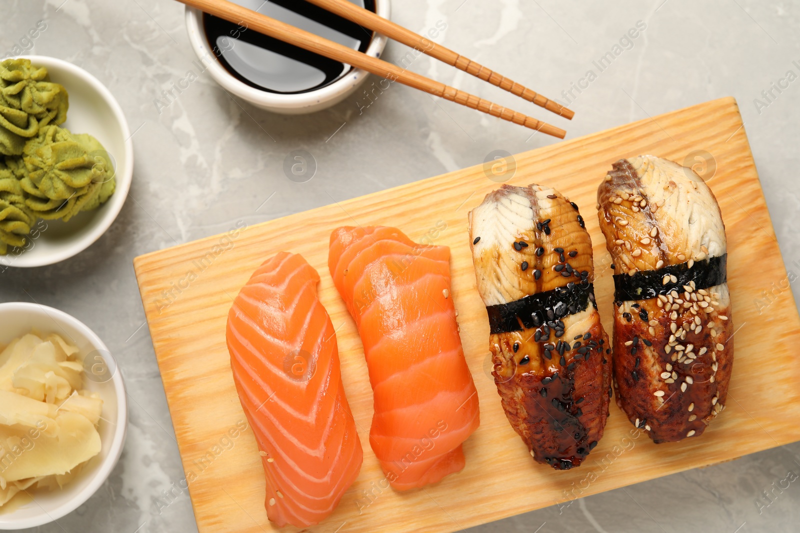 Photo of Delicious nigiri sushi, soy sauce, wasabi, ginger and chopsticks on light grey marble table, flat lay