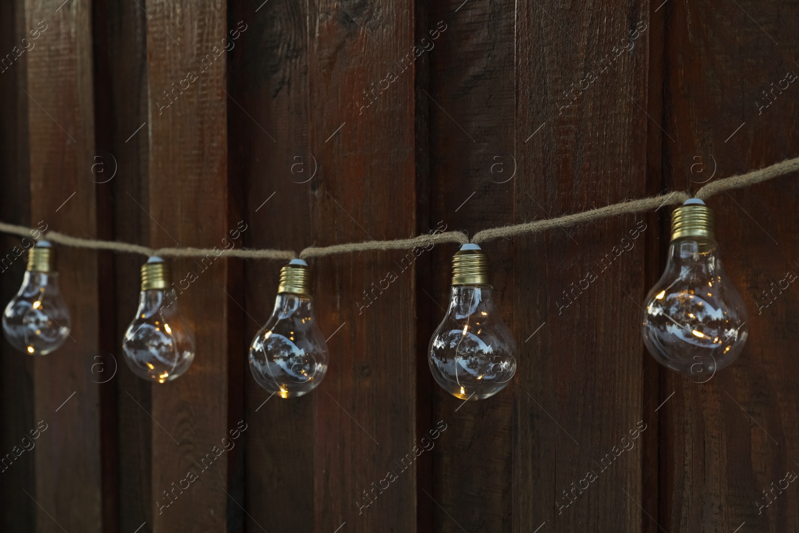 Photo of Garland of lamp bulbs hanging on wooden wall. String lights