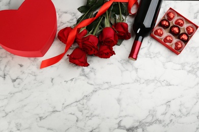 Photo of Flat lay composition with beautiful red roses and bottle of wine on white marble background, space for text. Valentine's Day celebration