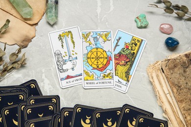 Photo of Tarot cards with gemstones and old book on grey table, flat lay