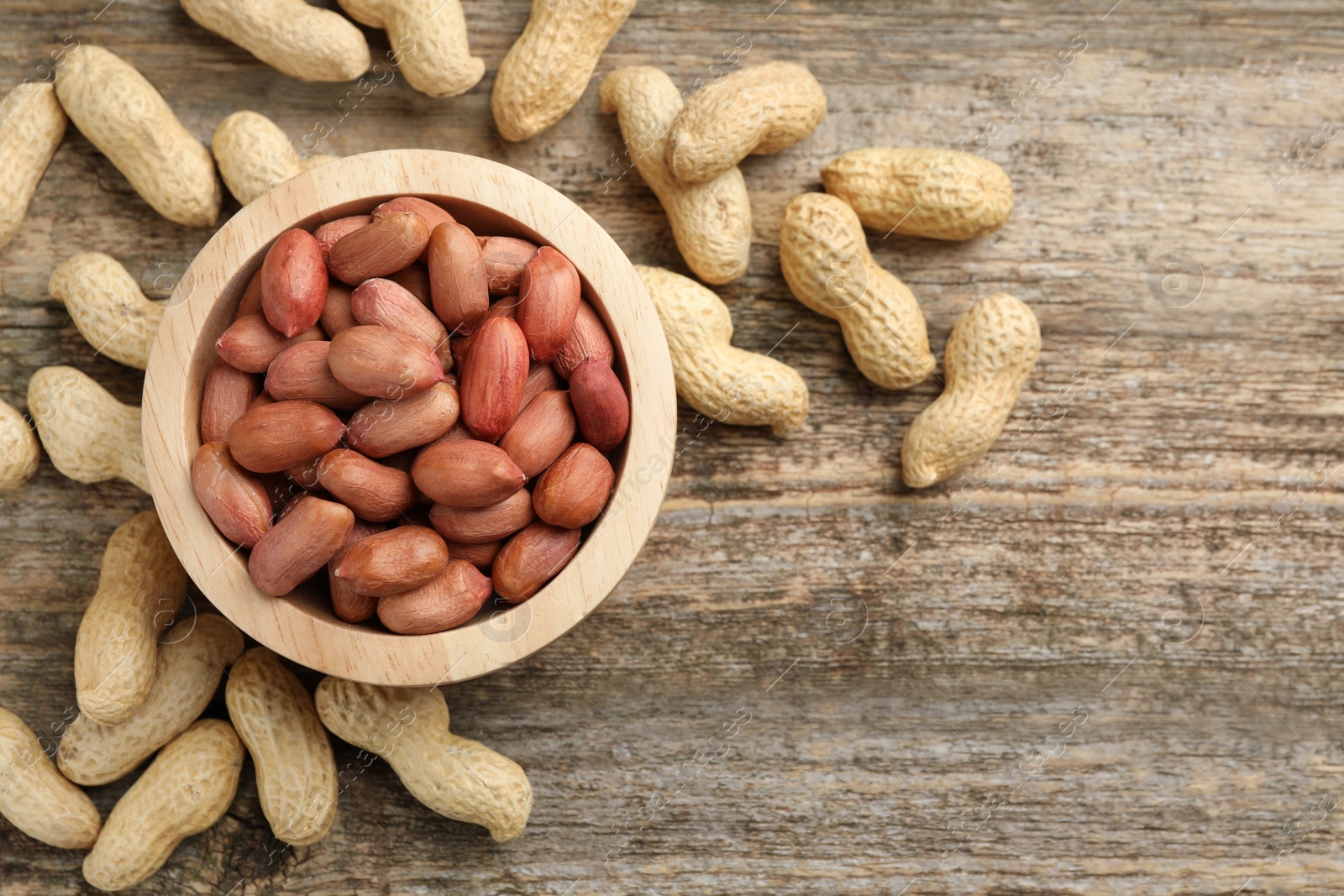 Photo of Fresh unpeeled peanuts in bowl on wooden table, top view. Space for text