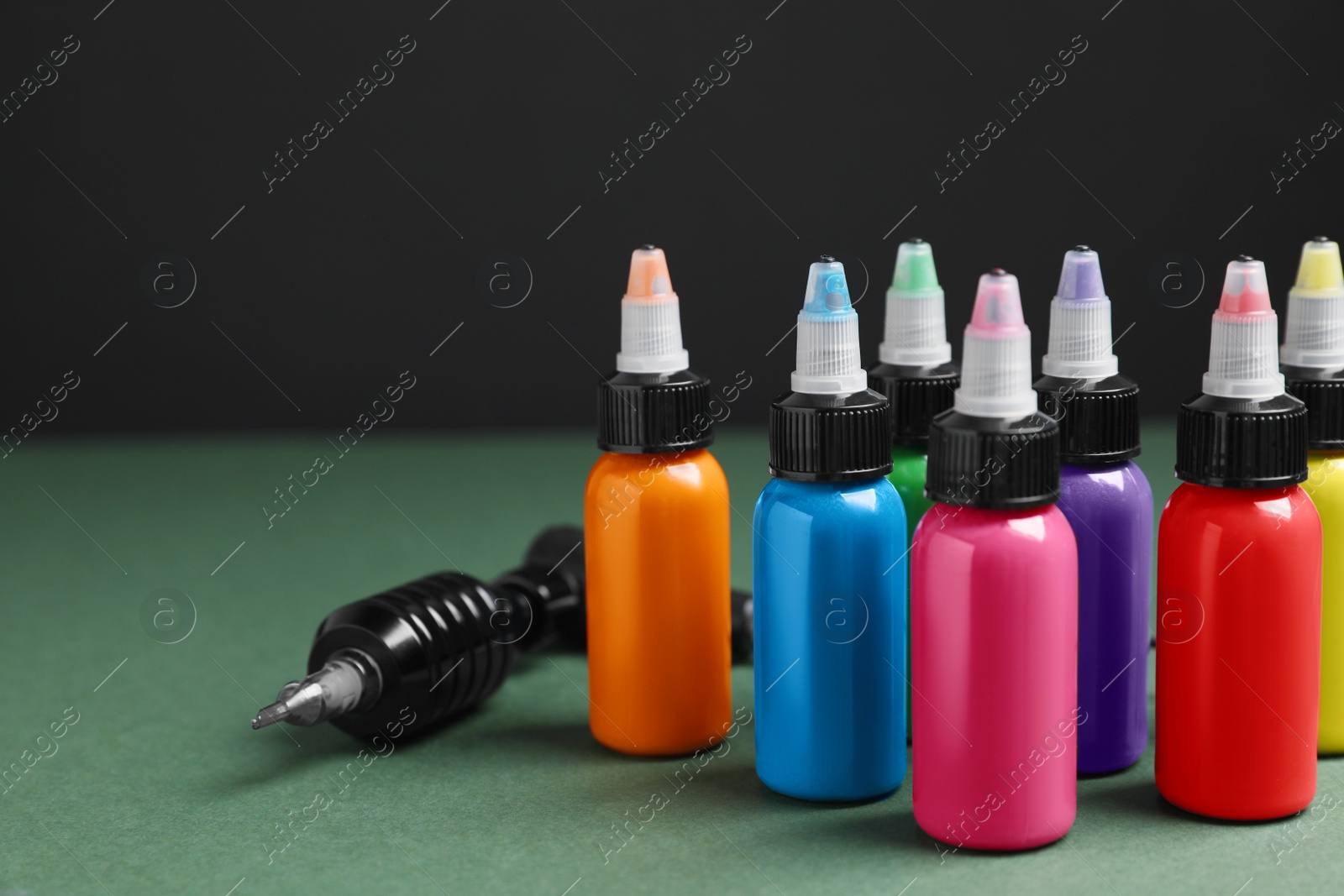 Photo of Tattoo machine and colorful inks on dark green table against black background, closeup