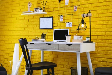 Stylish home office interior with comfortable workplace near yellow brick wall