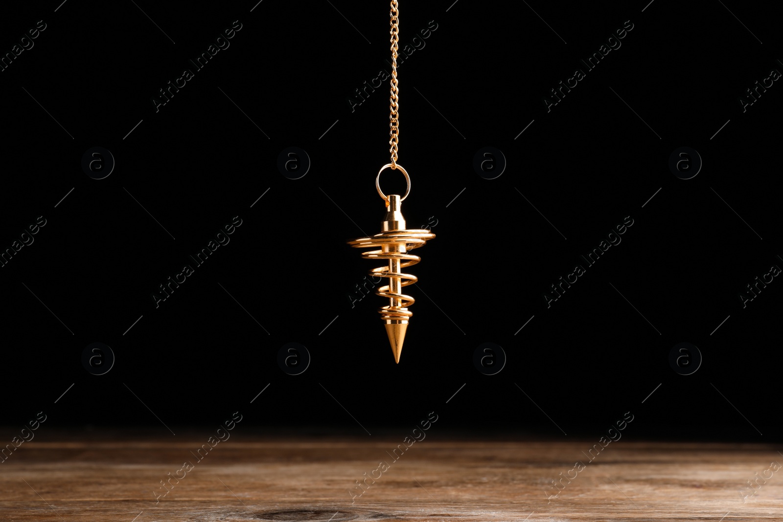 Photo of Stylish pendulum above wooden table on black background. Hypnotherapy session