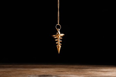 Stylish pendulum above wooden table on black background. Hypnotherapy session
