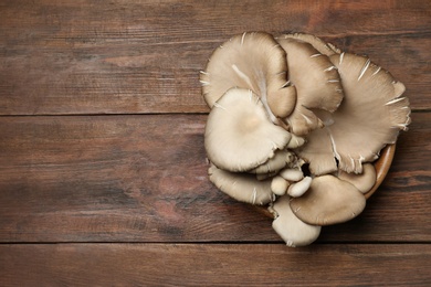 Photo of Bowl of delicious organic oyster mushrooms on wooden background, top view with space for text