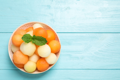 Photo of Melon balls and mint in bowl on light blue table, top view. Space for text