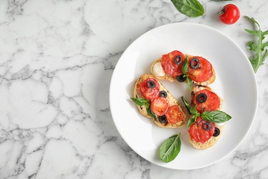 Photo of Plate of delicious tomato bruschettas on white marble background, top view. Space for text