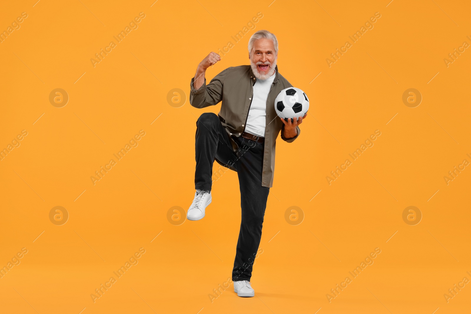 Photo of Emotional senior sports fan with soccer ball on yellow background