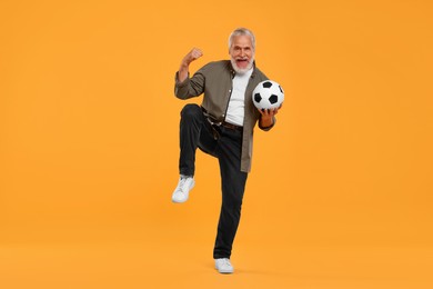Photo of Emotional senior sports fan with soccer ball on yellow background