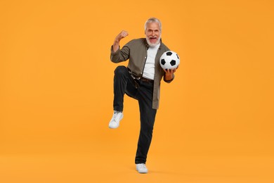 Emotional senior sports fan with soccer ball on yellow background