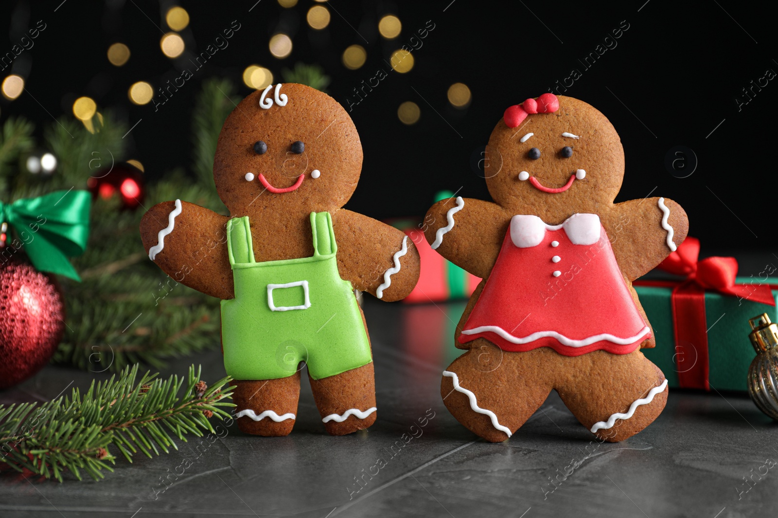 Photo of Gingerbread couple on black table against blurred lights, closeup
