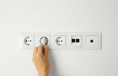 Photo of Woman putting plug into socket indoors, closeup