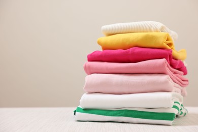 Photo of Stack of folded clothes on wooden table against beige background, space for text