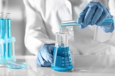 Photo of Scientist pouring light blue liquid from test tube into flask in laboratory, closeup