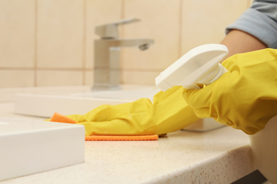 Photo of Woman cleaning counter with detergent and rag in bathroom, closeup