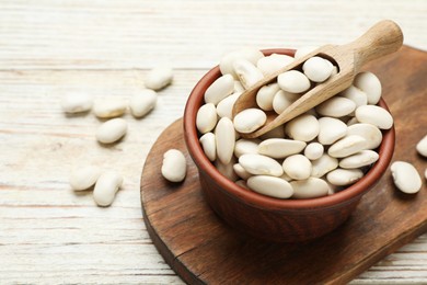 Photo of Bowl and scoop with uncooked white beans on wooden table, space for text