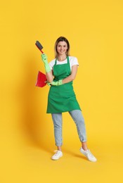 Photo of Young woman with broom and dustpan on orange background