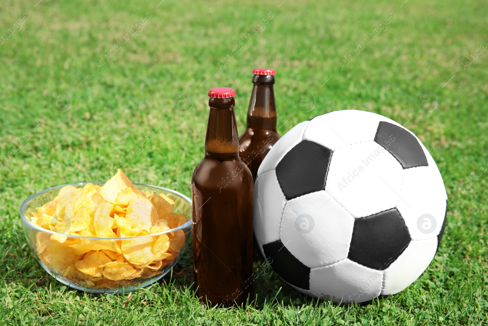 Photo of Soccer ball with beverage and chips on green football field grass